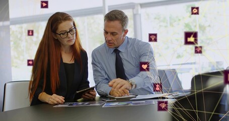 Colleagues pointing and studying tablet after digital icons appearing, updating charts by window