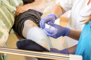 Nurse performing wound dressing change on patient leg during clinical nursing care in hospital ward
