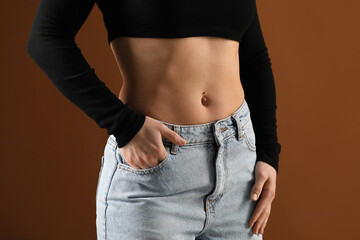 Fototapeta premium Woman with belly button piercing on brown background, closeup