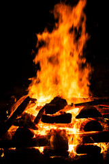 Narrow focus of a crackling bonfire at night in Brazil. Orange flames dance among stacked wood, illuminating the darkness. Sparks fly up, creating a fascinating visual spectacle.