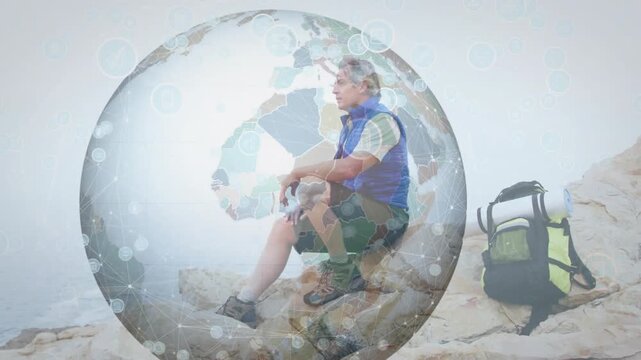Mature man sitting on rocky ledge, timed globe surrounding him, fading in, visualizing travel map