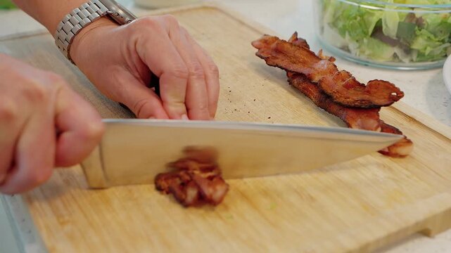 close up of a person chopping crispy fried bacon on a wooden cutting board