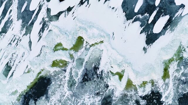 Top-down drone close-up of frozen Baltic Sea ice with snow streaks, translucent cracks, and green-tinted patches creating abstract winter textures and natural patterns.
