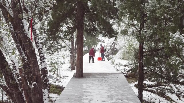 Rear view of two unknown cleaners using snow shovels to clear the snow on the timber trail in Changping valley in Siguniang mountains in heavy snowing day, 4k slow motion footage.
