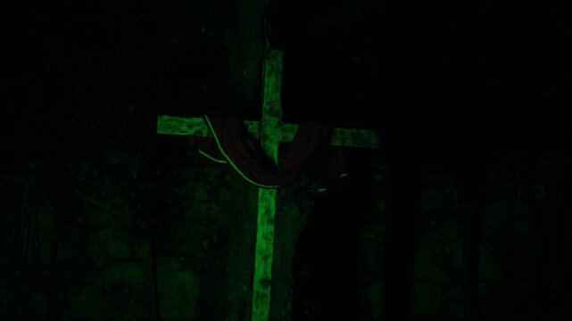 slow push in toward wooden cross with draped cloth as green light washes over the surface emerging from deep darkness