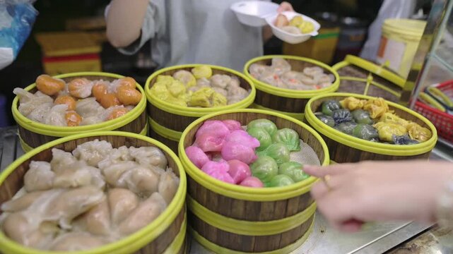 Individual Choosing Variety Of Steamed Buns And Dumplings From Baskets. Customer Carefully Selecting Lively And Colorful Traditional Asian Street Food Items From Bamboo Containers
