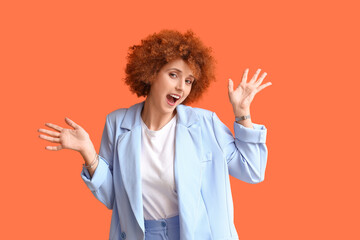 Happy redhead young woman with curly hair in suit on orange background