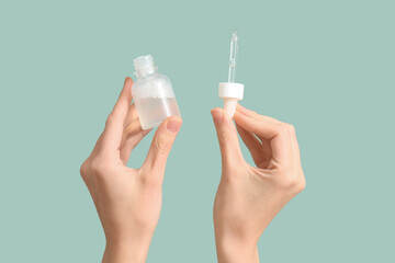 Female hands with bottle of cosmetic product on turquoise background