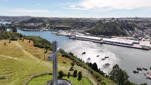 Cinematic aerial raising over the octagonal sanctuary of the 25-meter Monumental Cross on Tenglo Island to reveal the Reloncav&iacute; Sound, Puerto Montt city, and the busy artisanal harbor
