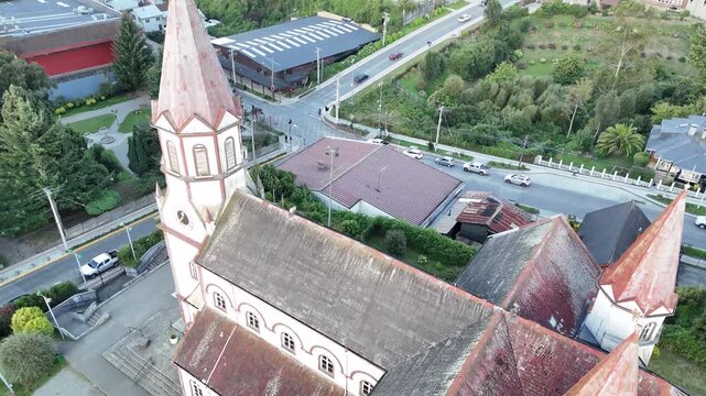 Aerial descending over the red spires and wooden roof of the Sacred Heart Church (Iglesia del Sagrado Coraz&oacute;n de Jes&uacute;s), revealing the street grid and urban life of Puerto Varas, Chile