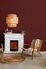 Naklejka premium Interior of stylish living room with cozy armchair, fireplace and glowing lamp near red wall