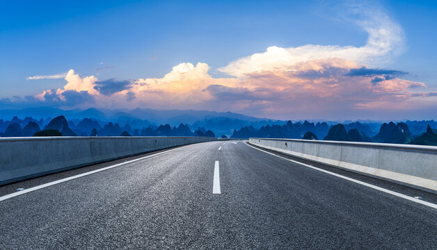 Empty asphalt road winding through karst mountain peaks under a sunset sky in Guilin, China. Road trip and travel concept.