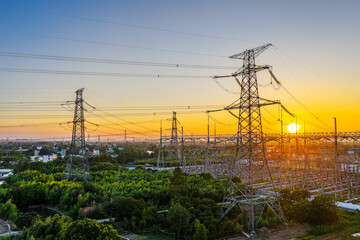 High voltage electrical substation and electricity transmission towers against a golden sunset sky. Power grid infrastructure for energy industry.