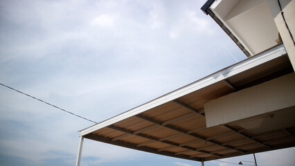 Low angle view of modern house roof and metal awning against cloudy blue sky with copy space, showing architecture details and eaves in daylight.
