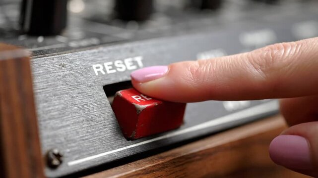 A close-up shot of a finger pressing a red reset button on a weathered metal surface