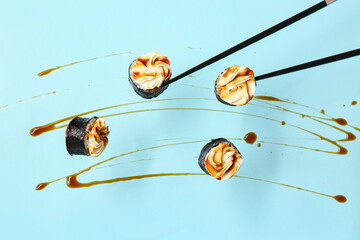 Tasty flying maki rolls, soy sauce and chopsticks on blue background © Pixel-Shot