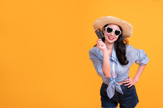 Happy Asian woman woman tourist showing credit card isolated on orange background.