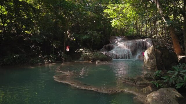 Beautiful tiered waterfall flowing through a lush tropical forest in Kanchanaburi, Thailand. Clear turquoise water cascades over limestone rocks creating a peaceful natural landscape.