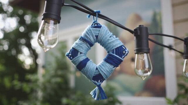 Diamond shaped yarn ornament hanging from string lights outdoors decoration rhombus