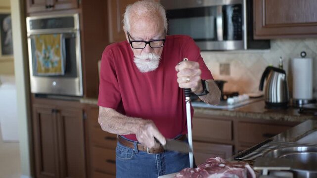 Senior man sharpens kitchen knives while getting ready to cook in the home kitchen with focus and care.