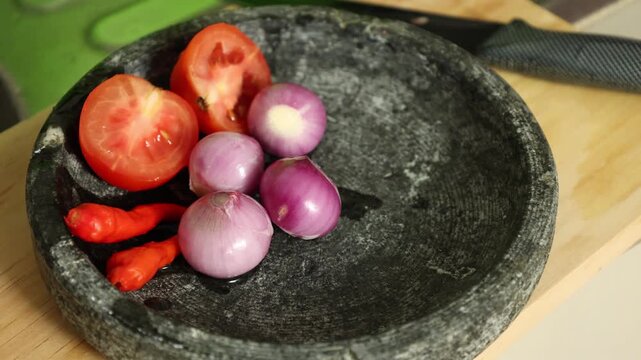 Red Chilies, red union, tomato, and Salt on stone ware (cobek), ingredients for making traditional Indonesian Sambal Tomat or Spicy Tomato Sauce. 
