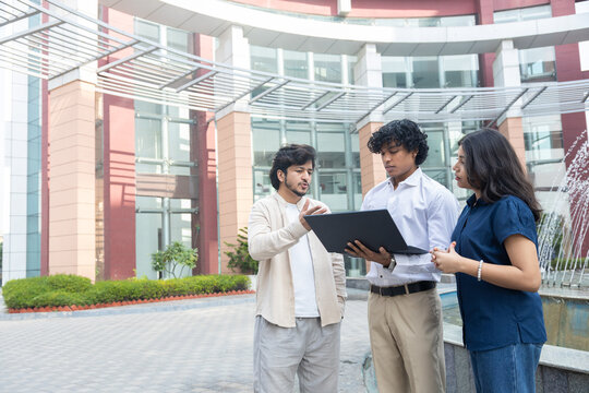Young indian entrepreneurs or business professionals discussing work, sharing ideas and do project using laptop outdoor office building, teamwork and corporate lifestyle.