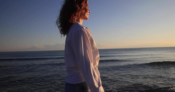 A happy young woman walking at the beach against the sunset during summer vacation. Slow motion