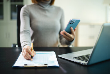 Fototapeta premium Confident professional woman using smartphone and laptop in a bright office. Concept of business technology