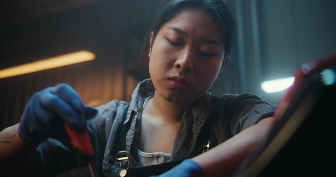 Female Works With Intense Focus, Carefully Using Screwdriver Repair Motorcycle in Modern Garage. Woman Concentrates on Precise Adjustments, Fully Immersed in Technical Process. Motorcycle Maintenance.
