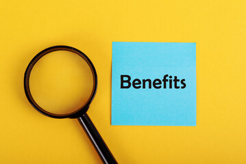 Magnifying glass focusing on a blue sticky note with the word "Benefits" on a vibrant yellow background. Concept of analyzing advantages, employee perks, research, and evaluation.