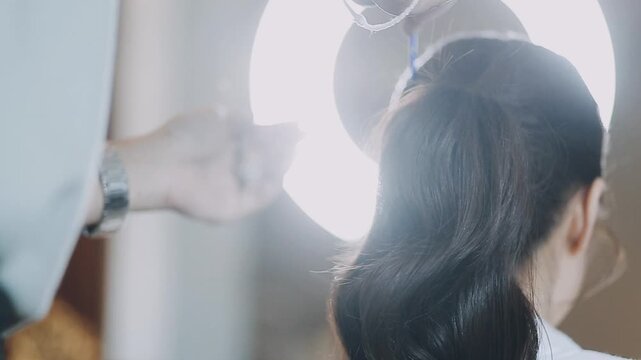 Female hairdresser makes hairstyle on young woman with brunette hair in salon.