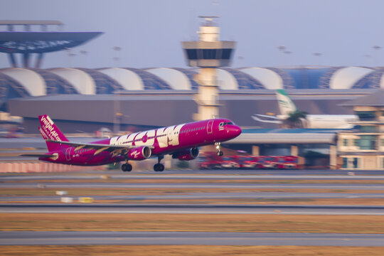 30-01-2026, Bangkok Thailand, Vibrant pink airplane takes off from bustling airport, with modern terminal and control tower in background. scene captures dynamic energy of air travel