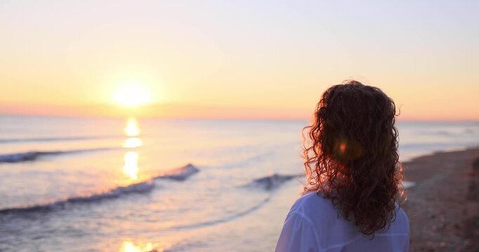 A happy young woman walking at the beach against the sunset during summer vacation. Slow motion