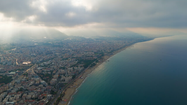 Alanya, Turkey. Aerial drone shot of urban coastline with Oba Beach, Tosmur Beach and sun rays through clouds over mountains and sea.. Aerial View