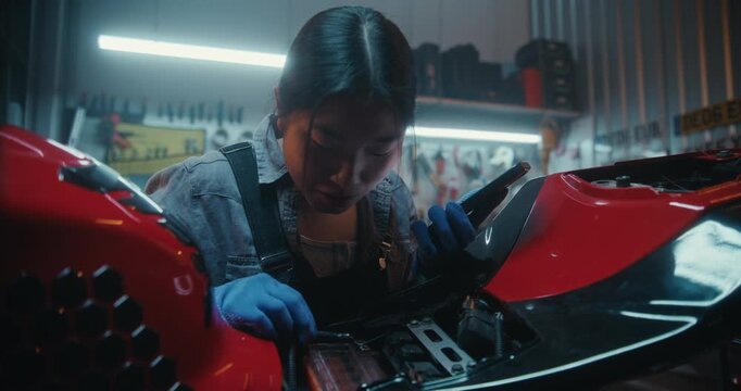 Young Woman Repairing Motorcycle in Modern Garage Uses Smartphone With Voice AI Assistant. Girl Describes Wiring Issues, Listens to Step By Step Instructions, Reconnecting According Digital Guidance.