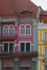Fototapeta premium Colorful art nouveau house stands on a street in Timisoara Romania. Curved red tiles and arched windows shape the playful facade. Pastel walls and balcony plants soften the street view.