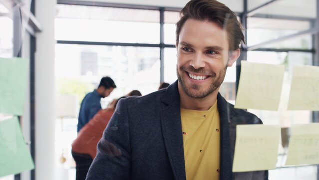 Thinking, man and reading notes on glass wall for planning, strategy and headline ideas. Smile, person and brainstorming with mindmap for agenda, timeline and information with publication reminder