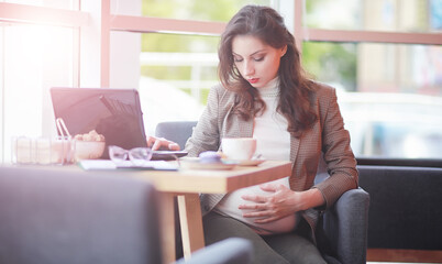 Pregnant woman working on computer in cafe