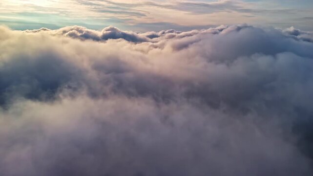 Aerial drone shot skimming above a dense cloud layer under a soft, diffuse grey sky. No horizon, no ground &mdash; only clouds filling the frame in all directions.