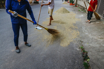 In Vietnam, workers sweep rice grains drying on a street in Hoa Lu Ancient Capital, Ninh Binh, Vietnam. This traditional method is used to preserve the rice, ensuring quality and preventing spoilage.