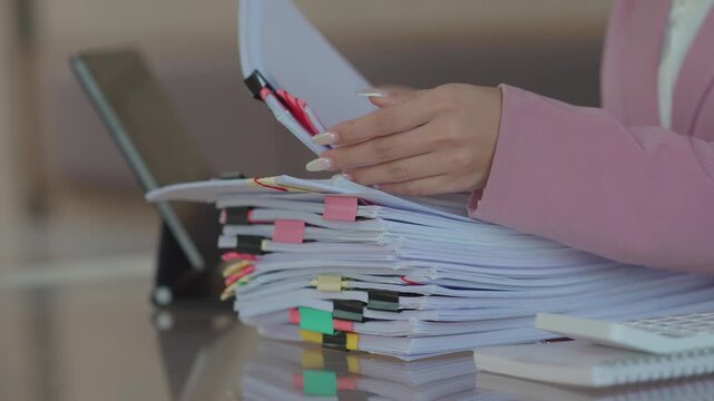 Close-up of a businesswoman reviewing a stack of organized documents with colorful tabs and clips at a desk, representing paperwork management, office organization, and administrative work.