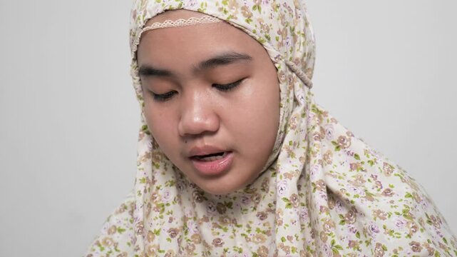 Peaceful young Asian Muslim teenage girl reading the Holy Quran in her bedroom for spiritual prayer and devotion, close up portrait