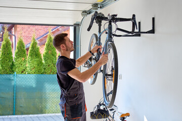 Man removes bicycle from wall rack inside garage for maintenance. Concept of home bicycle care,...