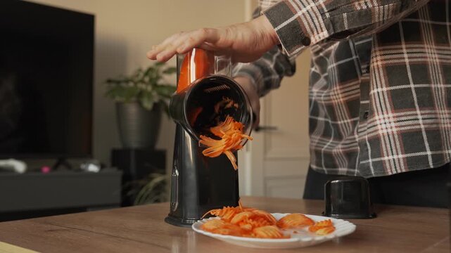The hands of a male householder slice carrots on a multi-slicer.