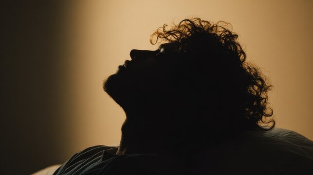A silhouette of a man looking upwards, bathed in warm light. His features are softly defined, with his eyes closed in a moment of reflection