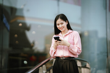 Fototapeta premium Smiling young woman talking on a smartphone outdoors in an urban area, expressing friendly communication, mobile connectivity, and modern digital lifestyle.