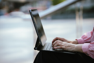 Close-up of hands typing on a tablet with keyboard outdoors, representing mobile work, remote productivity, digital technology, and modern flexible workspace.