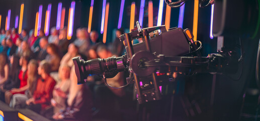 Professional broadcast camera filming live TV show with blurred audience and copy space