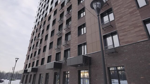 Multi-story building with brown facade and numerous windows forms dense rhythmic exterior grid. Architecture feels solid repetitive urban