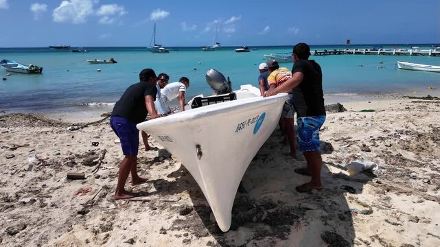Local fishermen push their boat into the sea in the Caribbean, Los Roques, Venezuela. Coastal life, teamwork, and traditional maritime activity
